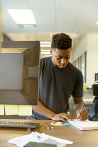 franchise-development-roles Young man working at a desk on a computer writing something down